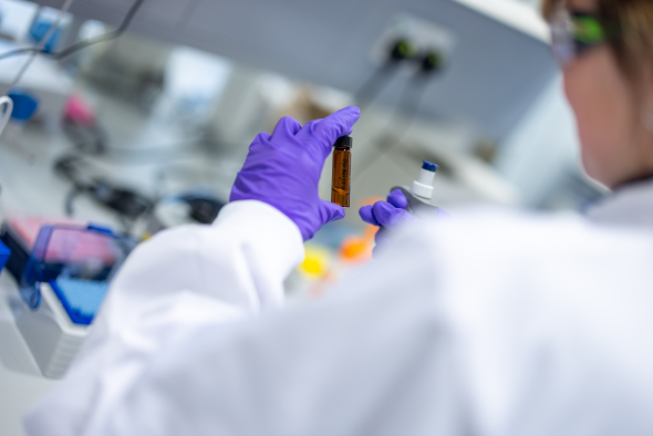 Purple gloved hand in white lab coat holding a brown glass vial