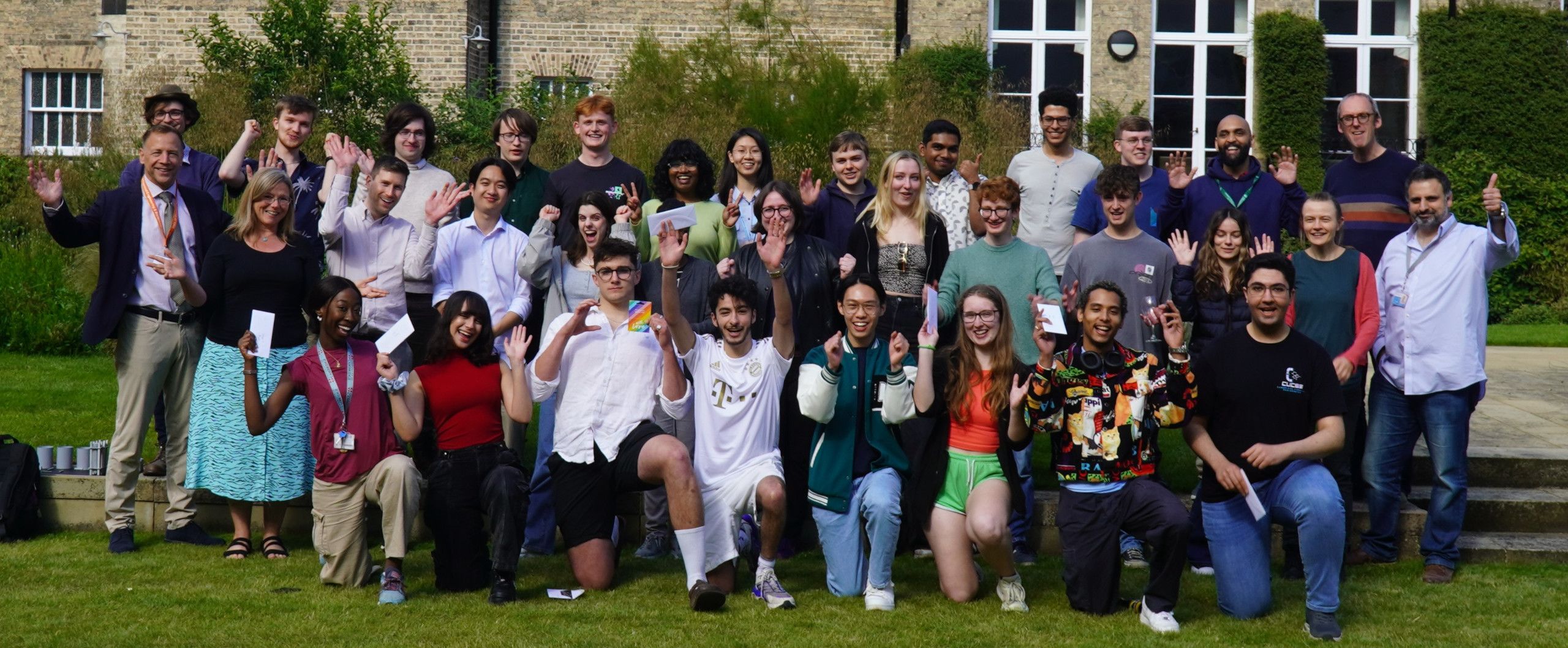 Students and teachers raise their arms in celebration outside in the sunshine