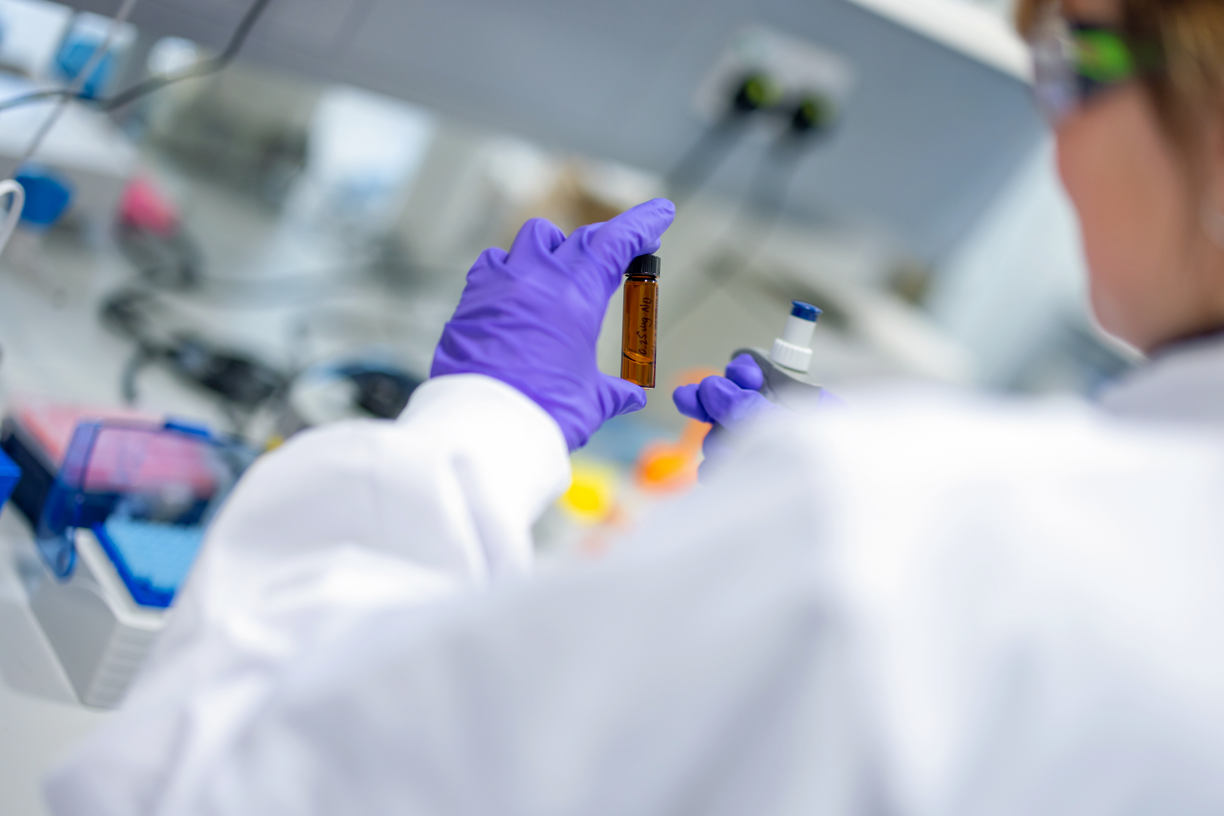 Purple gloved hand holding dark vial in laboratory setting