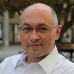 Bald, white man with glasses in white shirt smiling gently at the camera