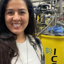 Woman smiling at the camera with long dark hair, with a bright yellow barrel in background with ICE on it