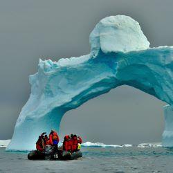 People in orange jackets on a boat looking at a frozen ice sculpture in antarctic