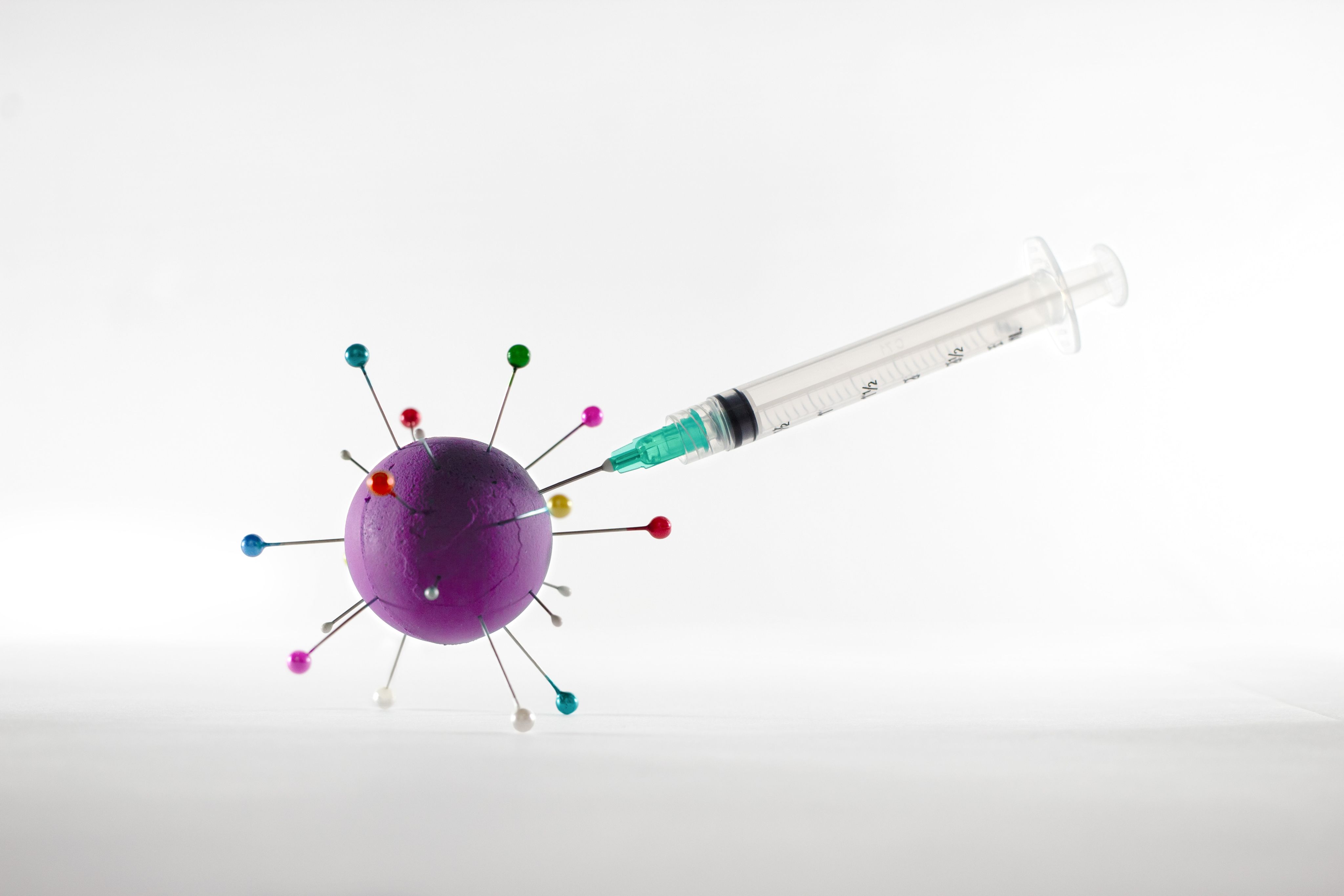 white and green syringe on white surface, injecting a vaccine into a representation of a virus